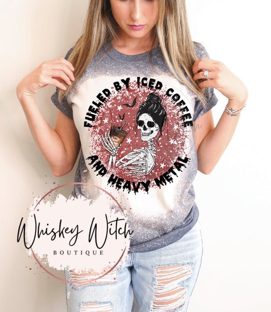 A bleached gray t-shirt with a red circle graphic featuring a skeleton holding a cup of iced coffee. The text around the graphic reads "Fueled by Iced Coffee and Heavy Metal". The text "Whiskey Witch Boutique" is printed below the graphic.
