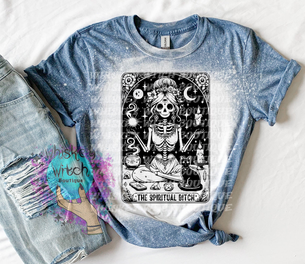 A bleached indigo  blue t-shirt with a black and white illustration of a skeleton woman with a cat and the text "The Spiritual Bitch".