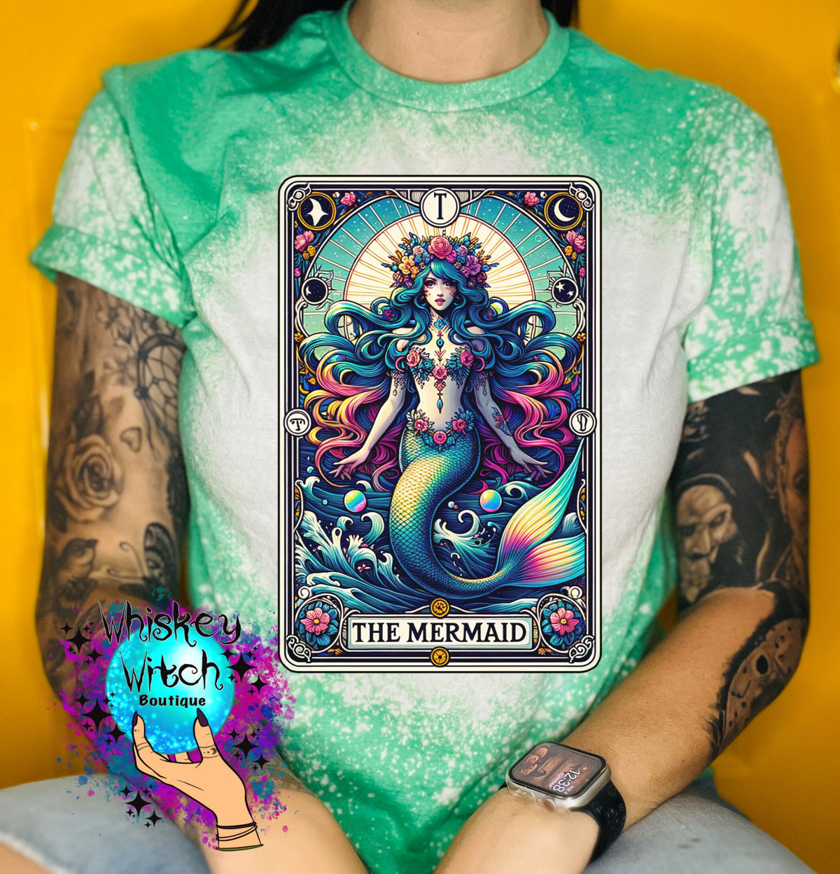 A green and white tie-dye t-shirt with a vintage tarot card design featuring a mermaid with a crown of flowers and the text "THE MERMAID".