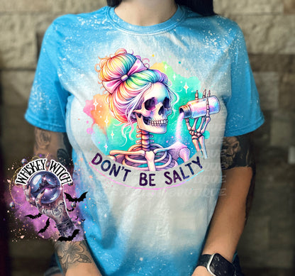 A bleached blue t-shirt with a colorful skeleton graphic pouring salt from a shaker. The text "Don't Be Salty" is printed on the shirt.