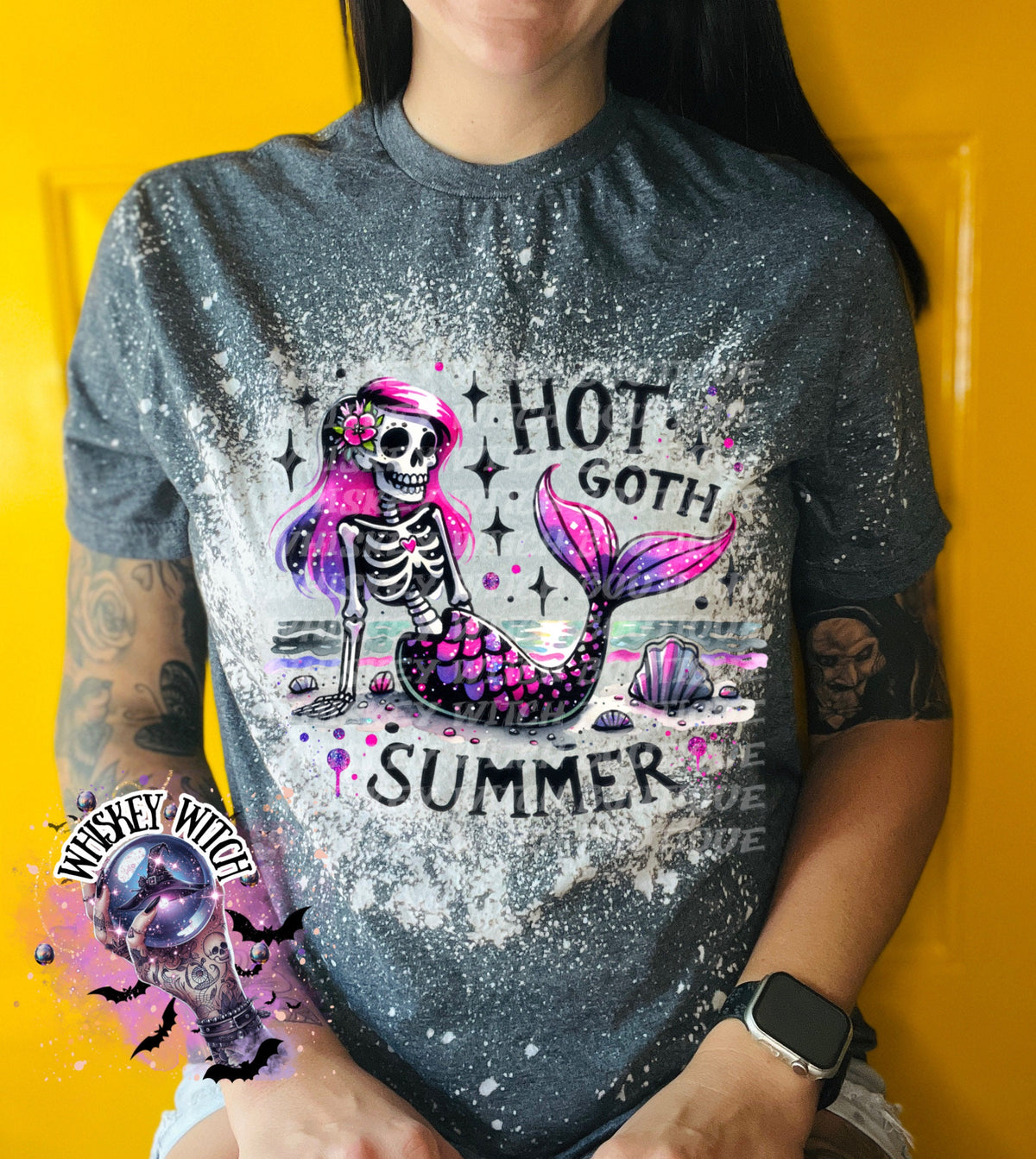 A gray t-shirt with a bleach-splattered design featuring a pink and purple skeleton mermaid with the text "Hot Goth Summer".