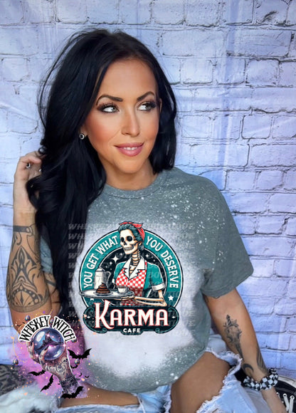 A green t-shirt with a bleached design featuring a skeleton wearing a red and white dress and holding a tray with a cup of coffee and a piece of cake. The text "You get what you deserve" is written around the skeleton. Below the skeleton is the text "Karma Cafe".