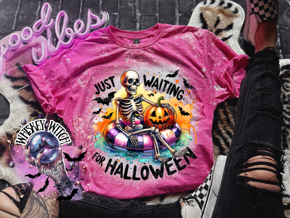 Pink t-shirt with a skeleton wearing a floatie and holding a pumpkin. The text on the shirt reads "Just Waiting for Halloween".