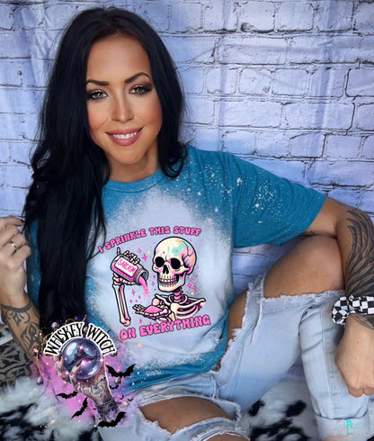 A Galapagos blue T shirt with bleach splattered design with a colorful skeleton holding a pouring a salt shaker that has the work ‘sarcasm’ on it with the words on the design ‘ I sprinkle this stuff on everything’