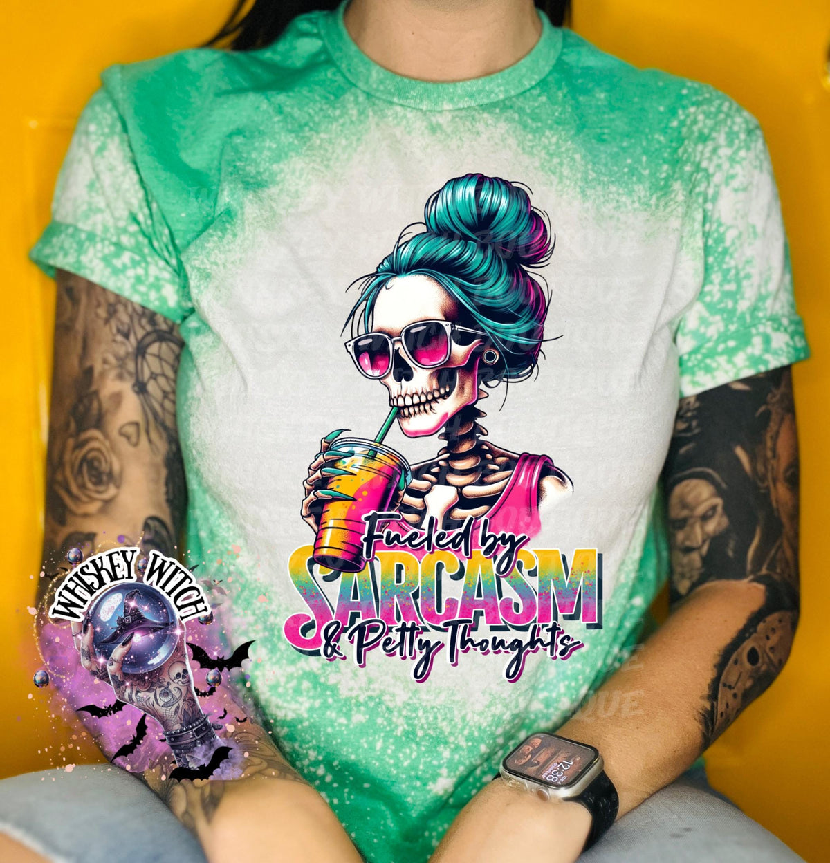 A green and white tie-dye t-shirt with a skeleton graphic holding a drink. The skeleton has blue hair and is wearing sunglasses. The text on the shirt reads "Fueled by Sarcasm & Petty Thoughts".