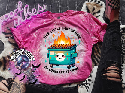 Pink t-shirt with a bleach-splattered design featuring a cartoon dumpster on fire with the text "This little light of mine I'm gonna let it shine".