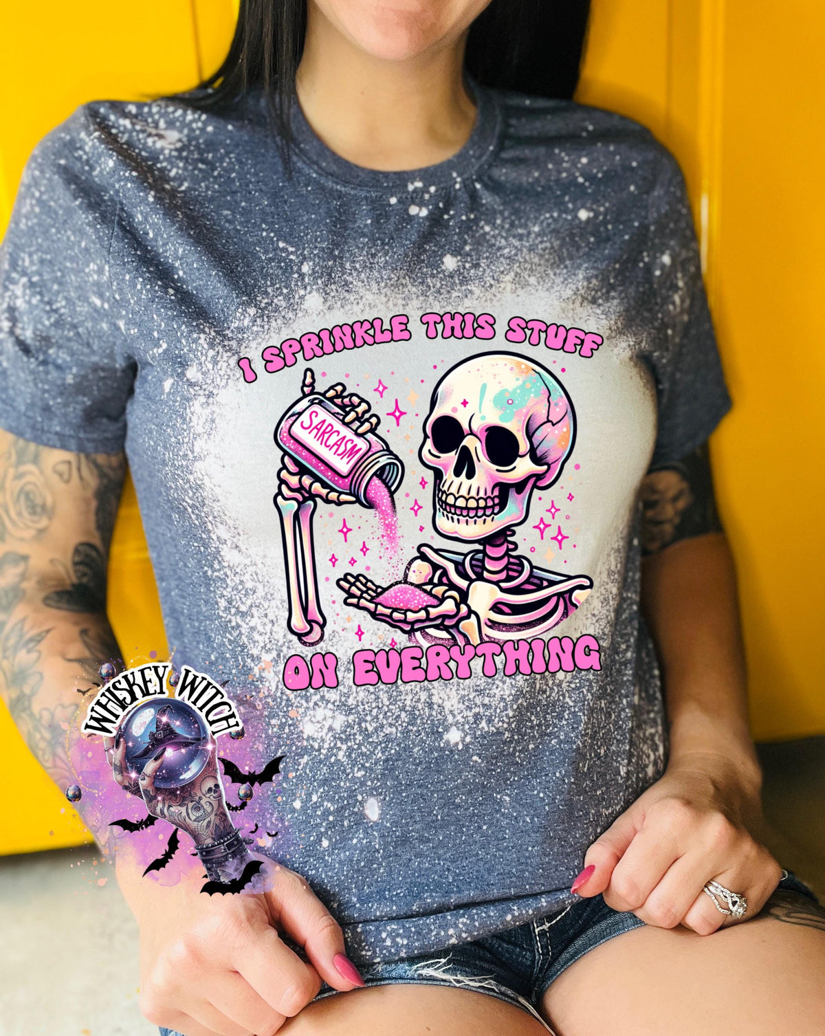 A navy blue T shirt with bleach splattered design with a colorful skeleton holding a pouring a salt shaker that has the work ‘sarcasm’ on it with the words on the design ‘ I sprinkle this stuff on everything’