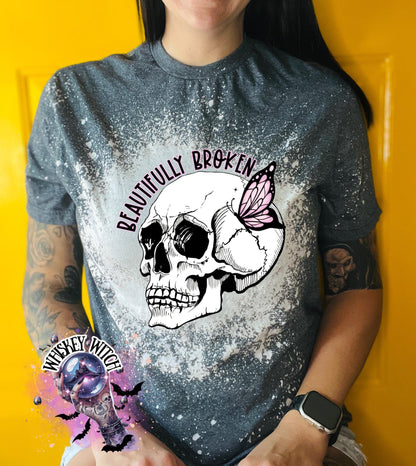Gray t-shirt with a bleached design featuring a skull with a butterfly on its side. The text "Beautifully Broken" is above the skull.