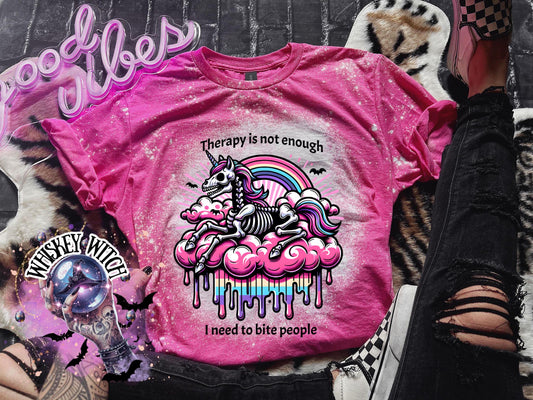 A pink and bleached design T shirt with a skeleton unicorn and a rainbow with a dripping colored cloud with the words “Therapy is not enough, I need to bite people.”