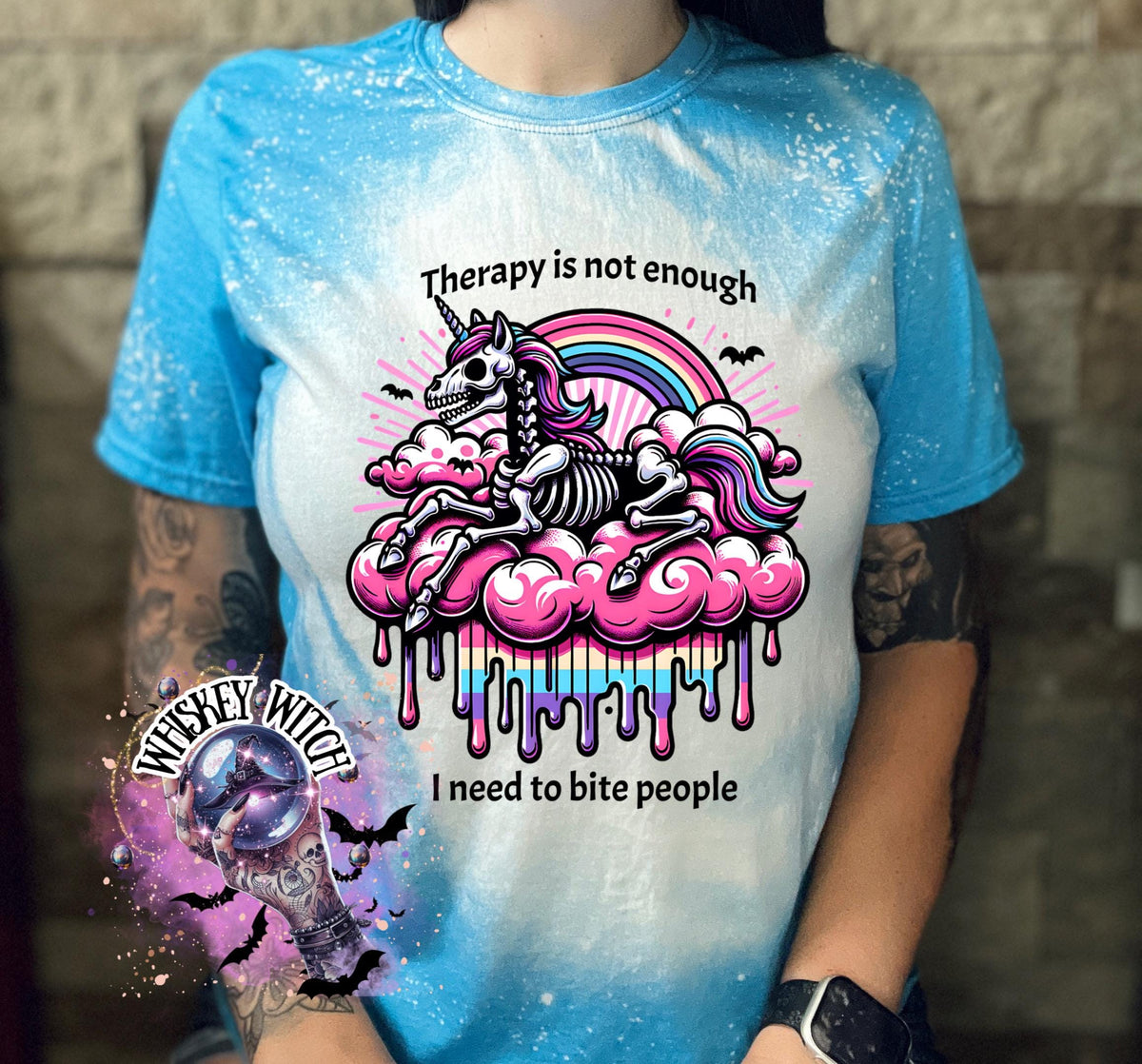 A sapphire blue  and bleached design T shirt with a skeleton unicorn and a rainbow with a dripping colored cloud with the words “Therapy is not enough, I need to bite people.”