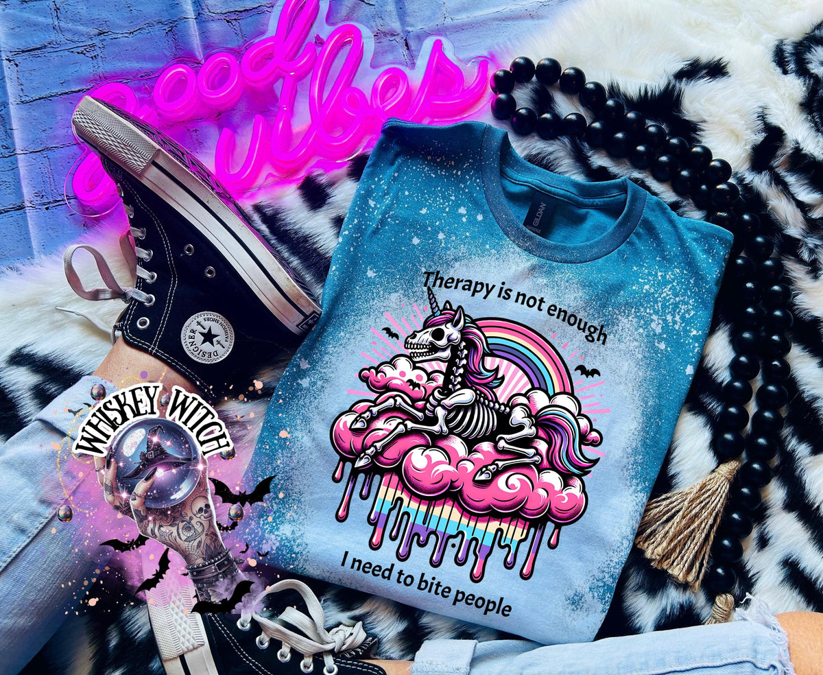 A Galapagos blue and bleached design T shirt with a skeleton unicorn and a rainbow with a dripping colored cloud with the words “Therapy is not enough, I need to bite people.”