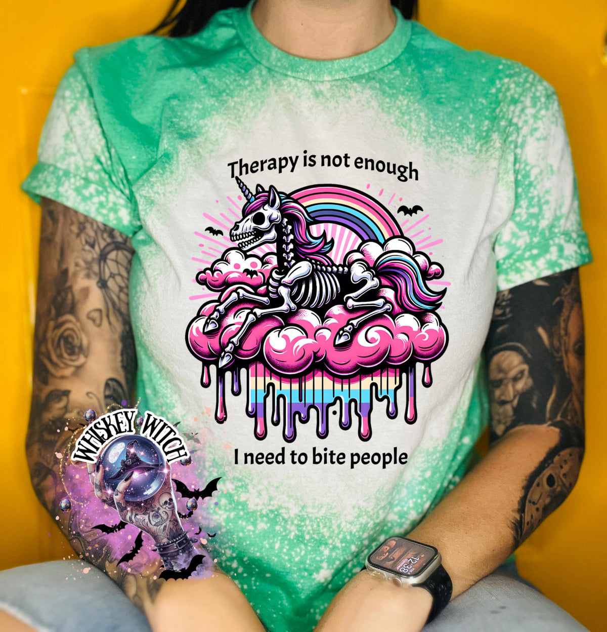 A green and bleached design T shirt with a skeleton unicorn and a rainbow with a dripping colored cloud with the words “Therapy is not enough, I need to bite people.”