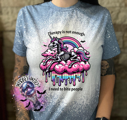 A indigo blue  and bleached design T shirt with a skeleton unicorn and a rainbow with a dripping colored cloud with the words “Therapy is not enough, I need to bite people.”