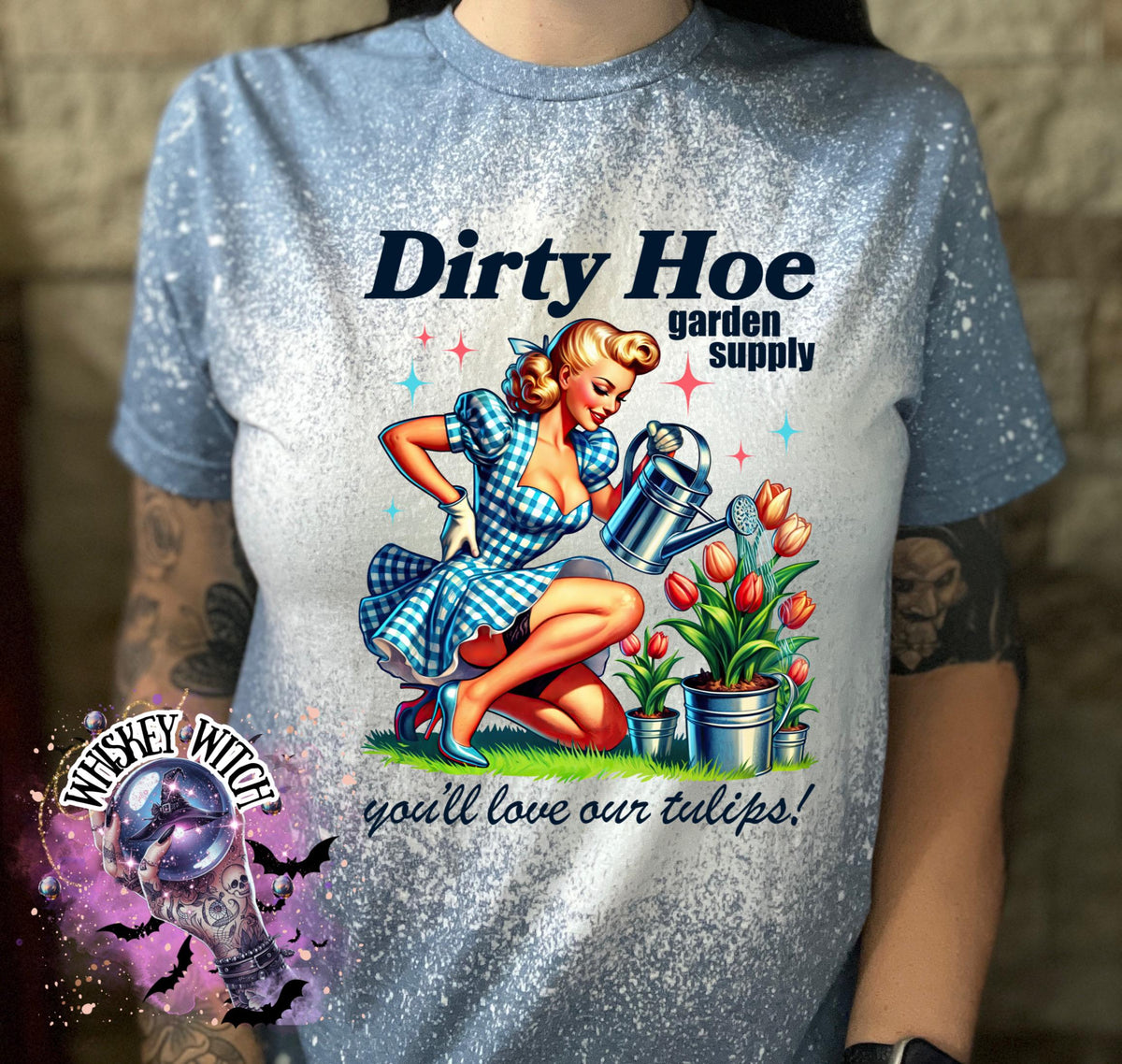 A blue t-shirt with a white bleach design featuring a pin-up style woman holding a watering can and a sign that reads "Dirty Hoe Garden Supply" and "You'll love our tulips!"