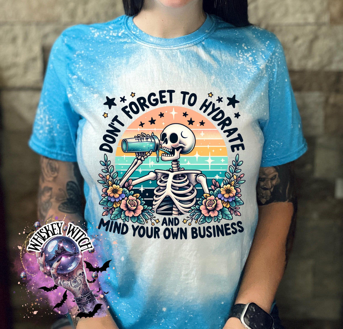 A sapphire blue and white bleached t-shirt with a skeleton drinking from a bottle and the text "Don't forget to hydrate and mind your own business".