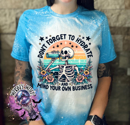 A sapphire blue and white bleached t-shirt with a skeleton drinking from a bottle and the text "Don't forget to hydrate and mind your own business".