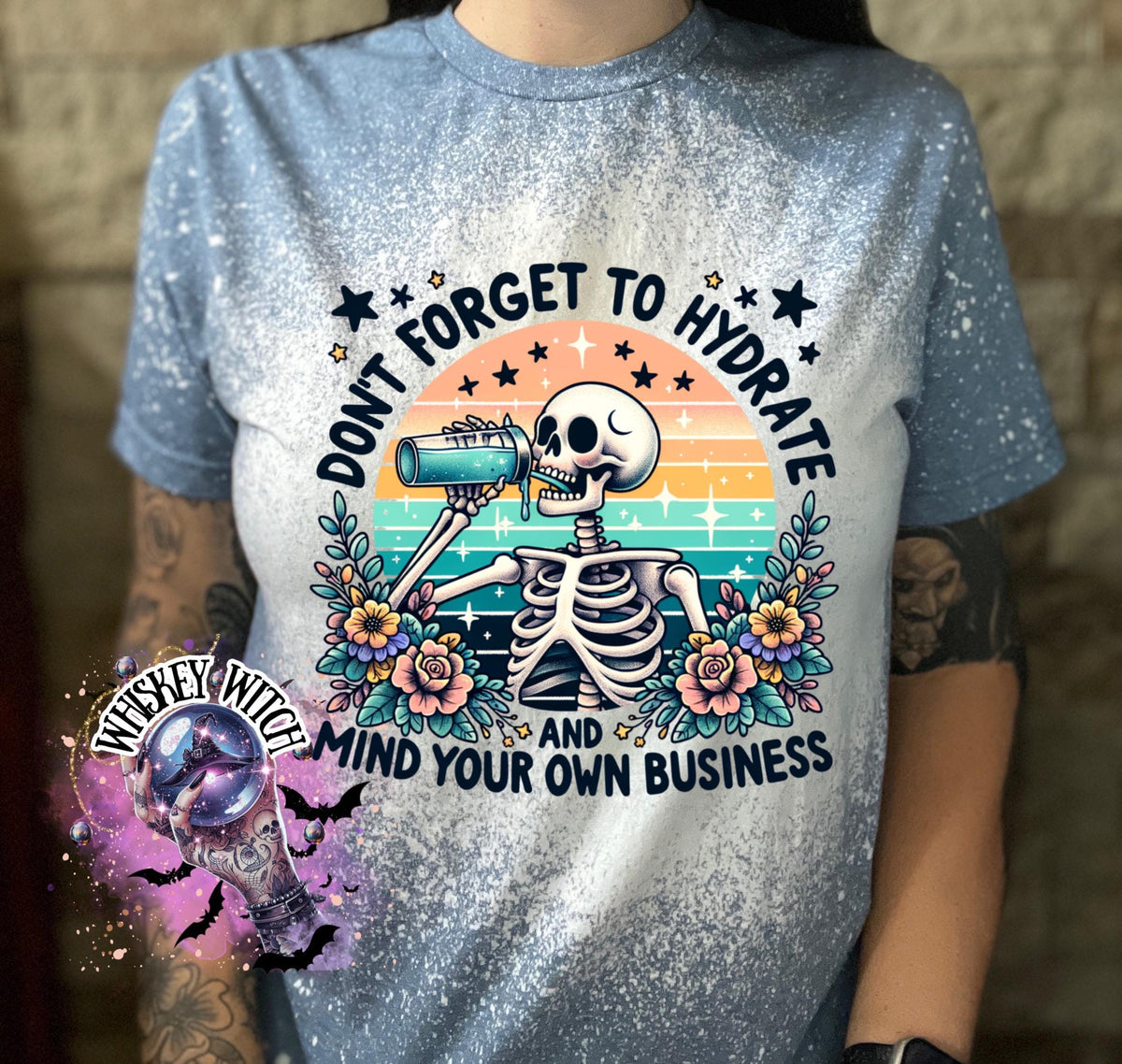 A blue and white bleached t-shirt with a skeleton drinking from a bottle and the text "Don't forget to hydrate and mind your own business".
