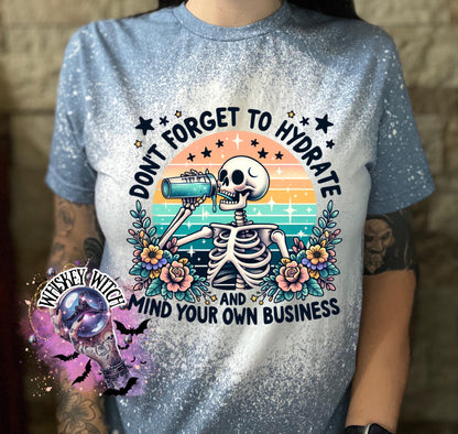 A blue and white bleached t-shirt with a skeleton drinking from a bottle and the text "Don't forget to hydrate and mind your own business".