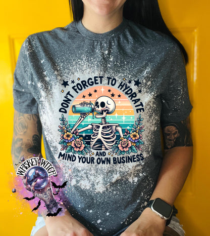 A grey and white bleached t-shirt with a skeleton drinking from a bottle and the text "Don't forget to hydrate and mind your own business".