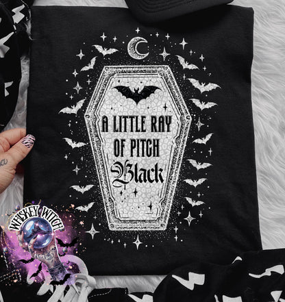 Black t-shirt with a gothic design featuring a coffin shape with the text "A Little Ray of Pitch Black". The design includes bats, stars, and a crescent moon, creating a spooky aesthetic.