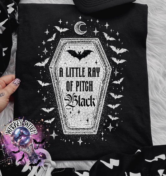 Black t-shirt with a gothic design featuring a coffin shape with the text "A Little Ray of Pitch Black". The design includes bats, stars, and a crescent moon, creating a spooky aesthetic.