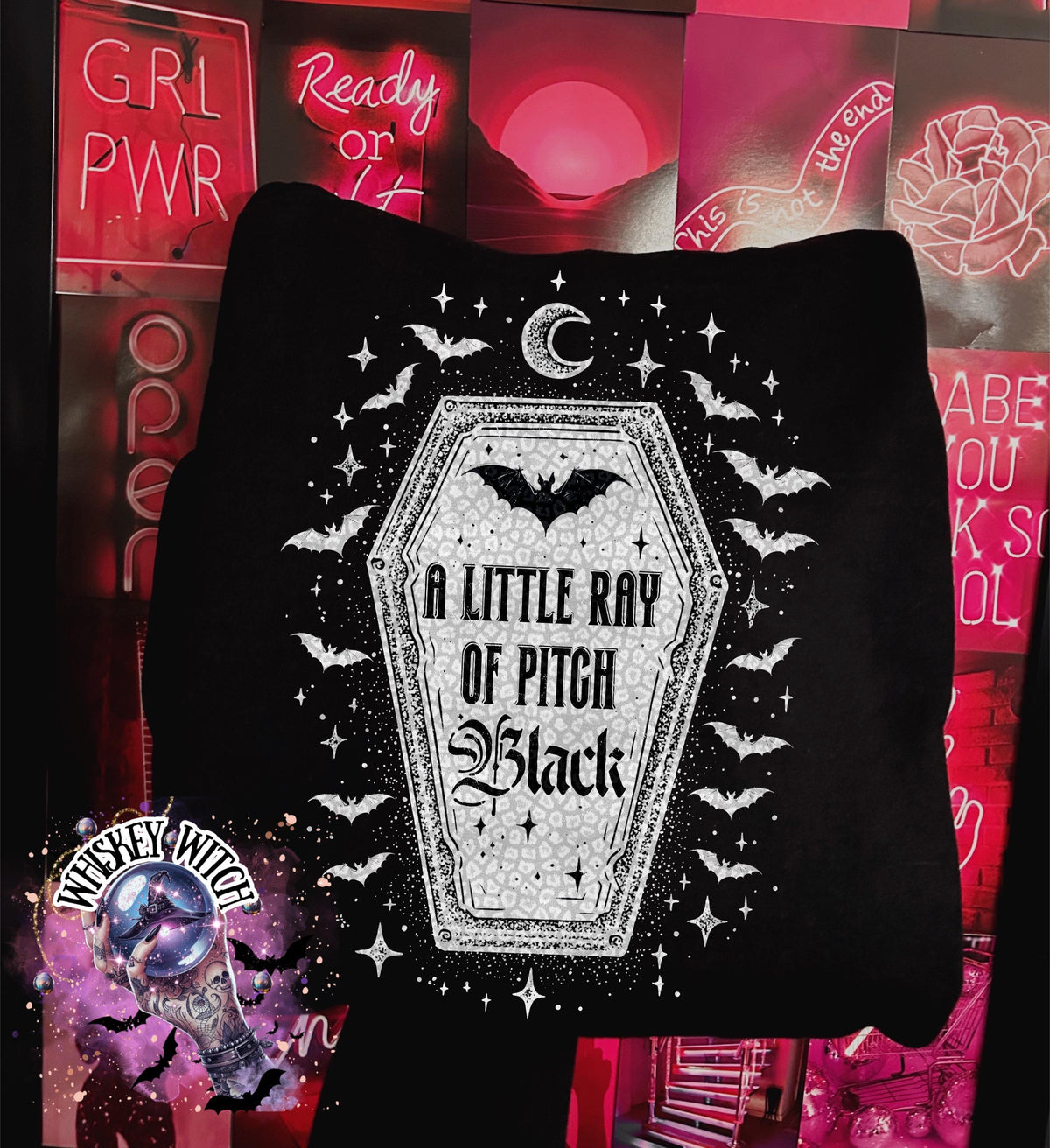 Black sweatshirt featuring a coffin design with bats, stars, and the text "A Little Ray of Pitch Black." The design is in white and gray, with a crescent moon at the top. The sweatshirt has a round neckline.