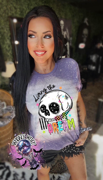 Hand-bleached purple graphic tee featuring a skull illustration, small stars, and the words “Living the Dream” with rainbow drip lettering.