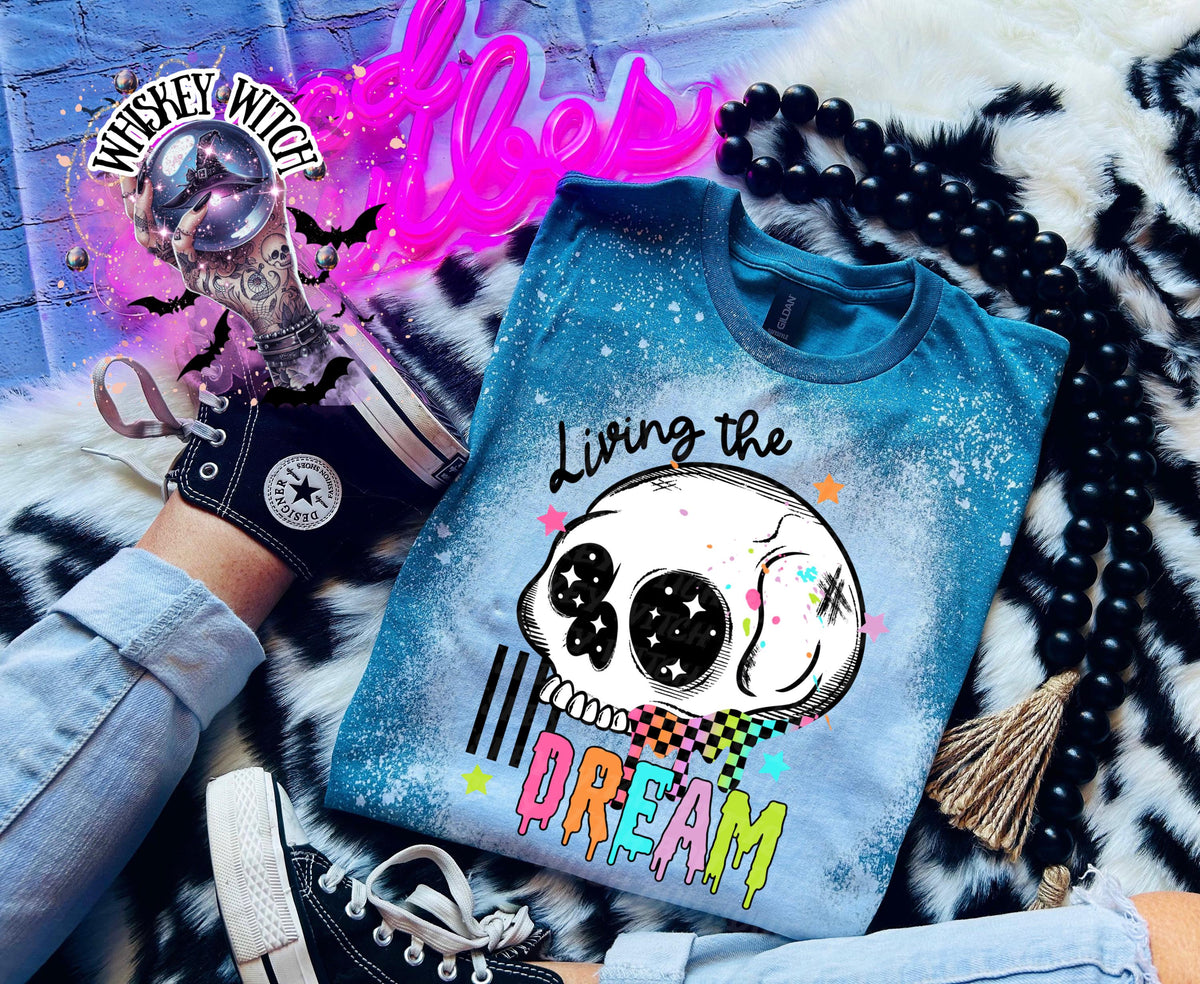 Hand-bleached teal  graphic tee featuring a skull illustration, small stars, and the words “Living the Dream” with rainbow drip lettering.