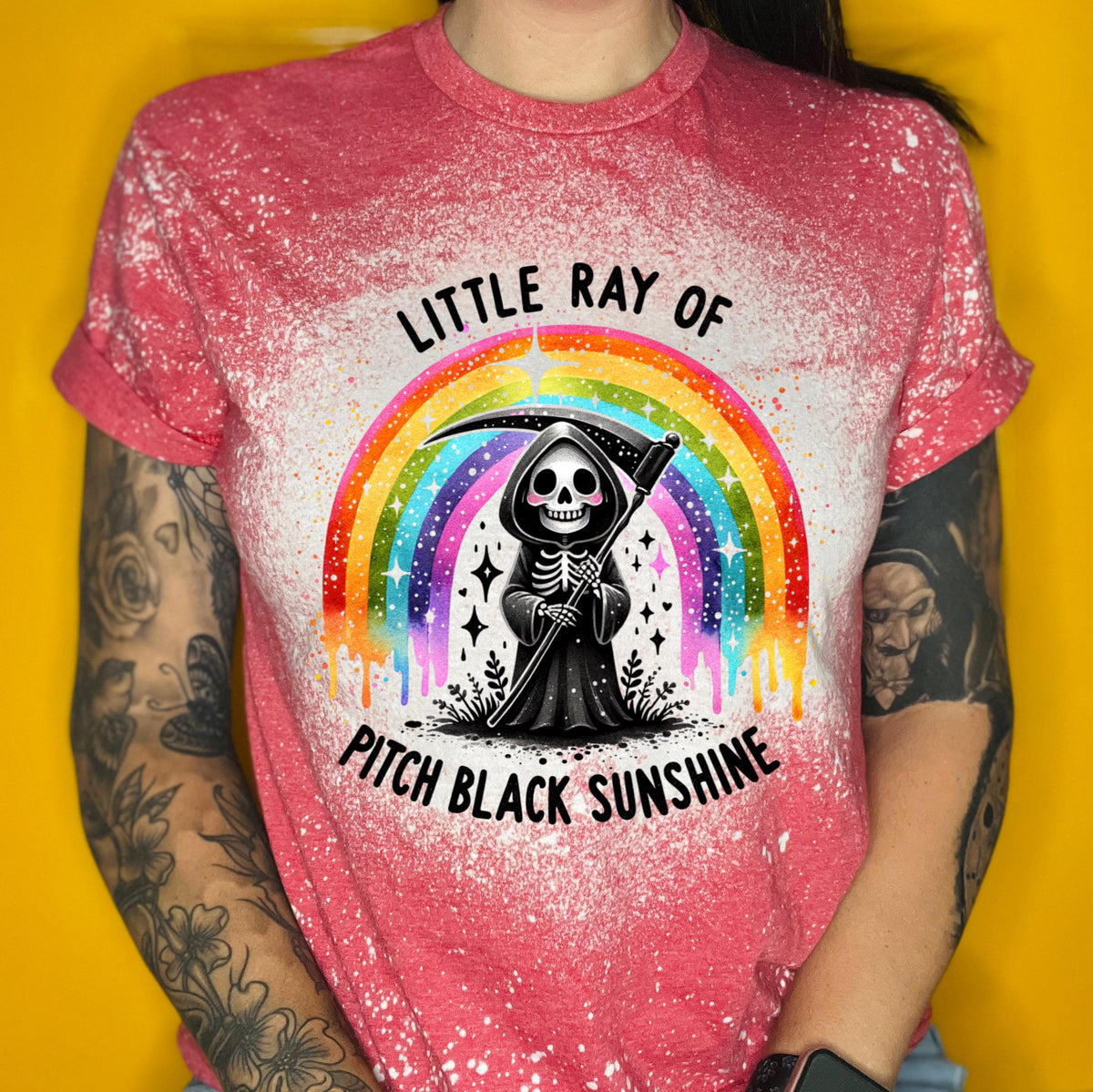 Close-up of bleach-wash tee showing dripping rainbow over a skeleton reaper holding a scythe with “Little Ray Of Pitch Black Sunshine” text.