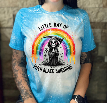 Close-up of bleach-wash tee showing dripping rainbow over a skeleton reaper holding a scythe with “Little Ray Of Pitch Black Sunshine” text.
