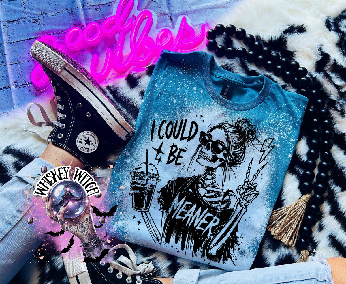 A Galapagos blue t-shirt with bleach white splatter effect with a graphic of a skeleton wearing sunglasses, holding a drink, and making a peace sign. The text on the shirt reads "I COULD BE MEANER.”