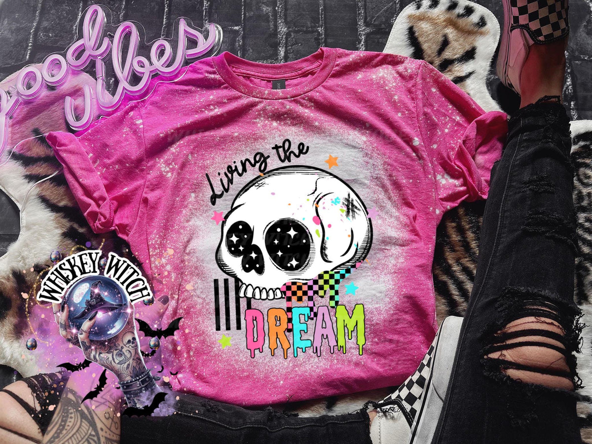 Hand-bleached Heliconia pink graphic tee featuring a skull illustration, small stars, and the words “Living the Dream” with rainbow drip lettering.