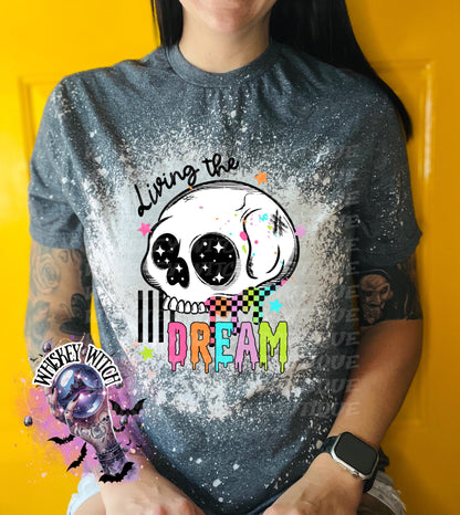 Hand-bleached dark Heather color  graphic tee featuring a skull illustration, small stars, and the words “Living the Dream” with rainbow drip lettering.