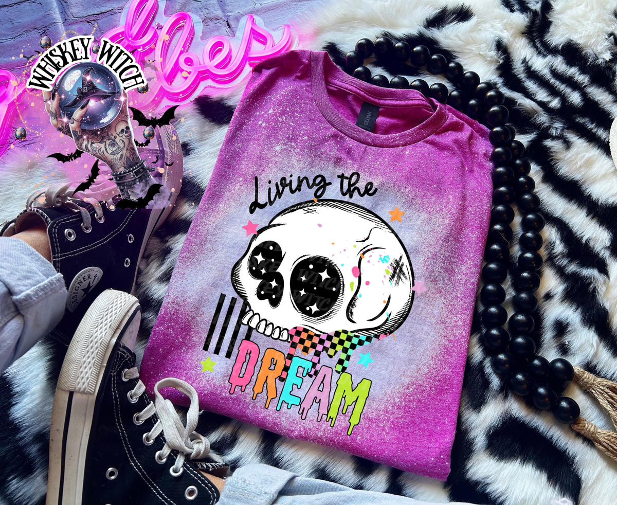 Hand-bleached Berry  graphic tee featuring a skull illustration, small stars, and the words “Living the Dream” with rainbow drip lettering.