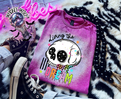 Hand-bleached Berry  graphic tee featuring a skull illustration, small stars, and the words “Living the Dream” with rainbow drip lettering.
