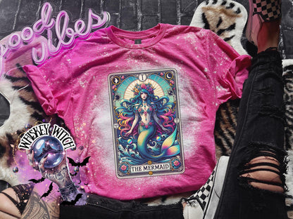 Mystical mermaid tarot card graphic centered on a Heliconia pink bleach-dyed shirt, photographed with neon pink sign and cozy background props.