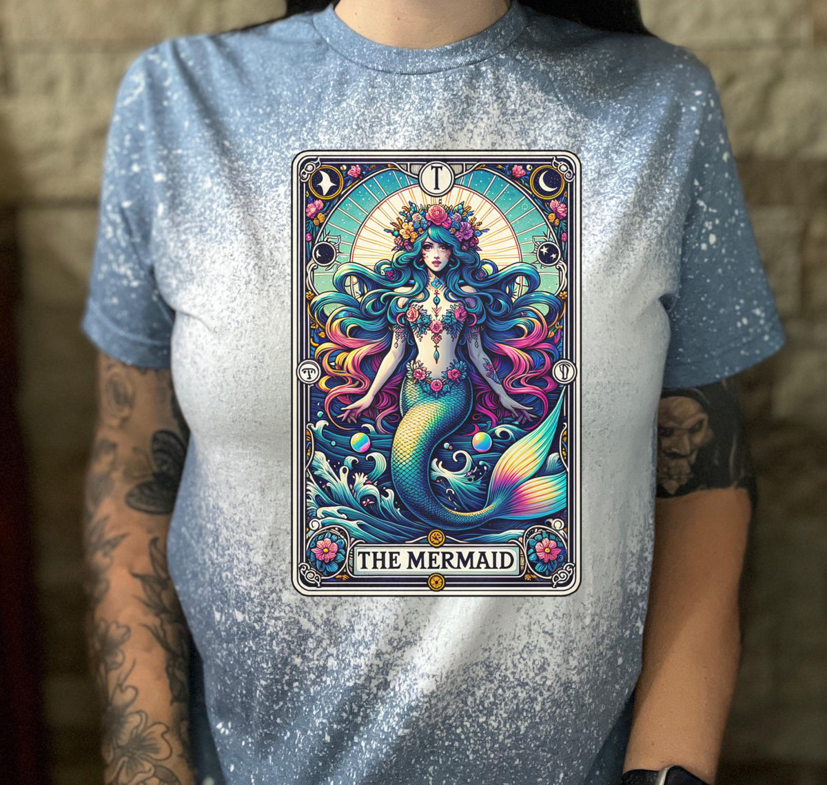 Mystical mermaid tarot card graphic centered on a indigo  bleach-dyed shirt, photographed with neon pink sign and cozy background props.