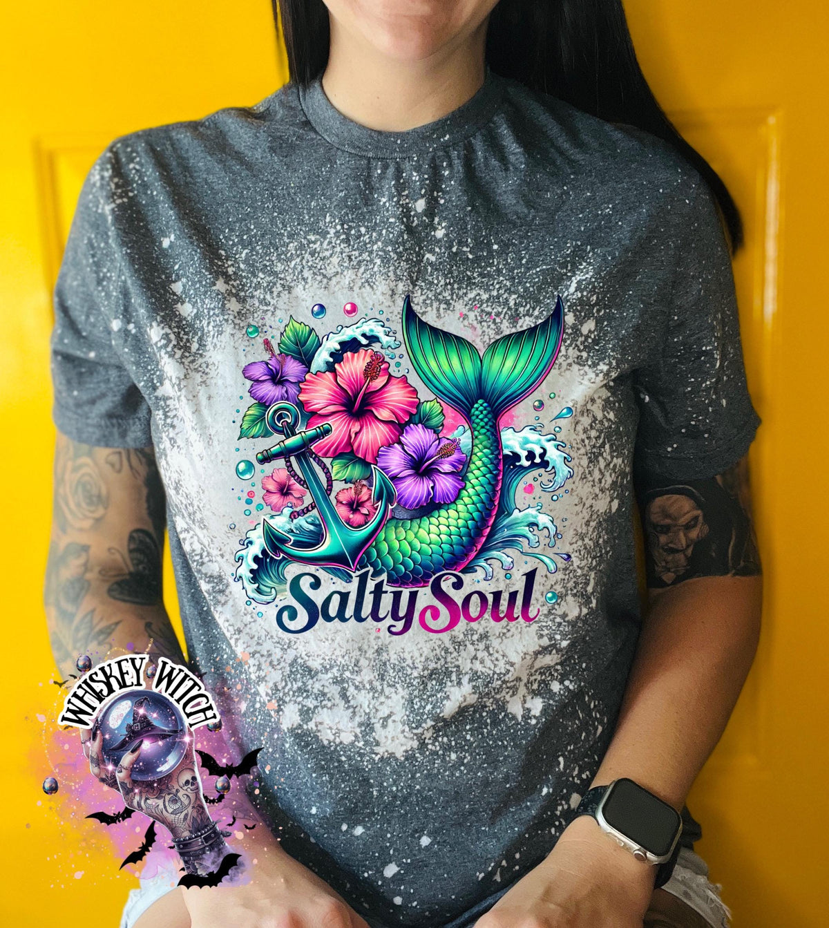 A dark Heather grey  t-shirt with a bleach splatter effect. The shirt features a colorful graphic of a mermaid tail, anchor, flowers, and the text "Salty Soul". The mermaid tail is green and blue.