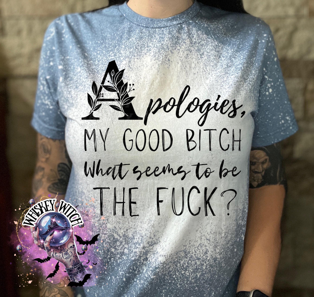 A light blue and white bleached t-shirt with the text "Apologies, MY GOOD BITCH What seems to be THE FUCK?" in black. The letter "A" is decorated with leaves. The shirt has short sleeves.
