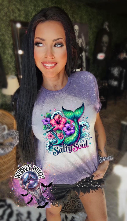 A purple   t-shirt with a bleach splatter effect. The shirt features a colorful graphic of a mermaid tail, anchor, flowers, and the text "Salty Soul". The mermaid tail is green and blue.