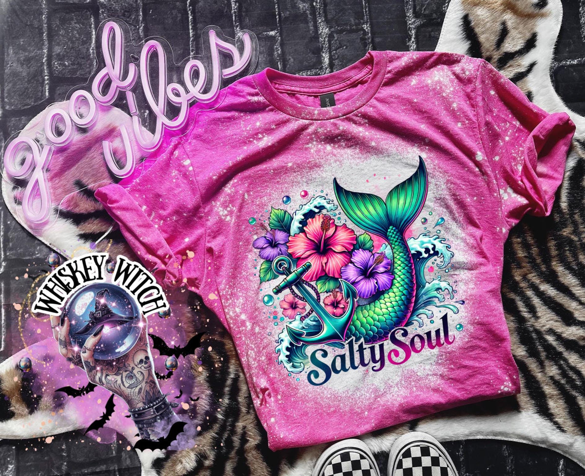 A pink  t-shirt with a bleach splatter effect. The shirt features a colorful graphic of a mermaid tail, anchor, flowers, and the text "Salty Soul". The mermaid tail is green and blue.