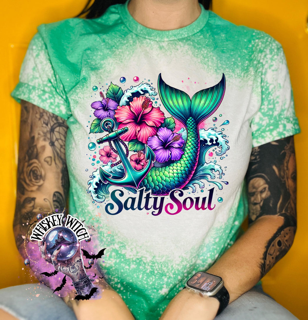 A green  t-shirt with a bleach splatter effect. The shirt features a colorful graphic of a mermaid tail, anchor, flowers, and the text "Salty Soul". The mermaid tail is green and blue.