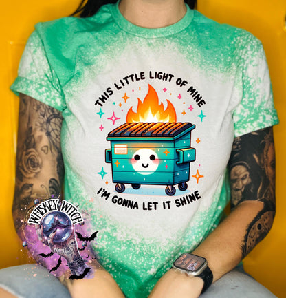 green t-shirt with a bleach-splattered design featuring a cartoon dumpster on fire with the text "This little light of mine I'm gonna let it shine".