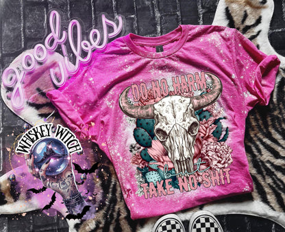 A pink t-shirt with a bleached effect, featuring a bull skull design with the text "DO NO HARM BUT TAKE NO SHIT". The shirt is decorated with floral and cactus elements.