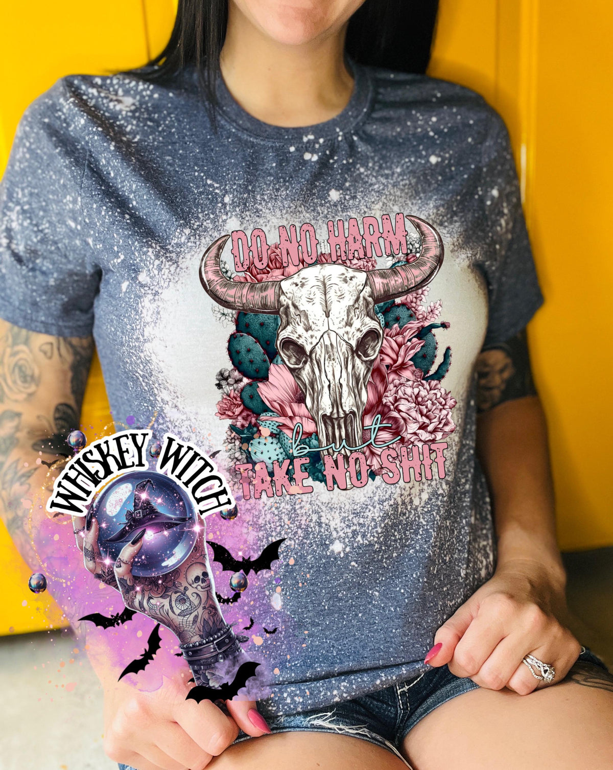 A blue and bleach effect  t-shirt featuring a bull skull graphic with the text "DO NO HARM BUT TAKE NO SHIT". The shirt also has a "Whiskey Witch" sticker with bats.