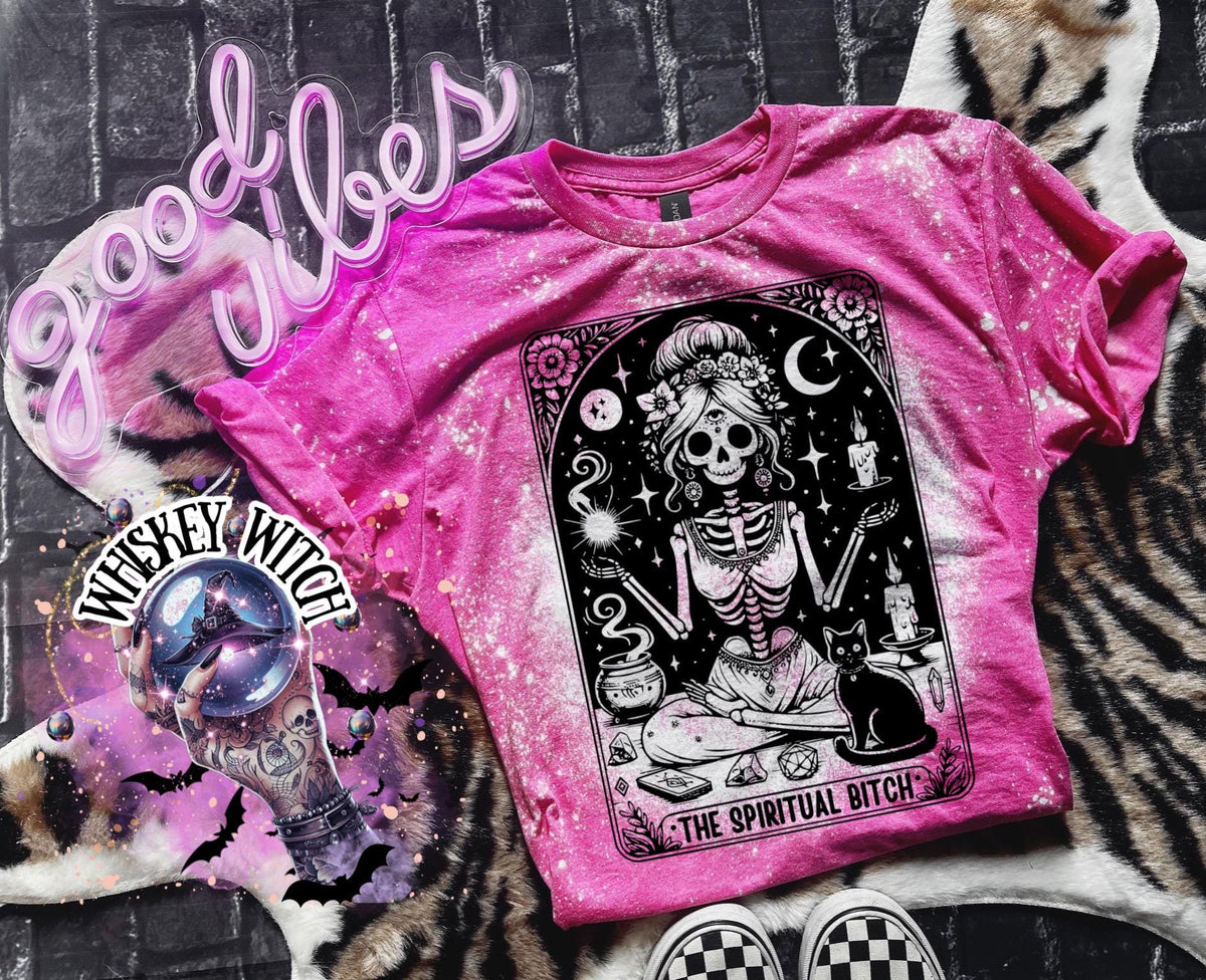 A bleached pink t-shirt with a black and white illustration of a skeleton woman with a cat and the text "The Spiritual Bitch".