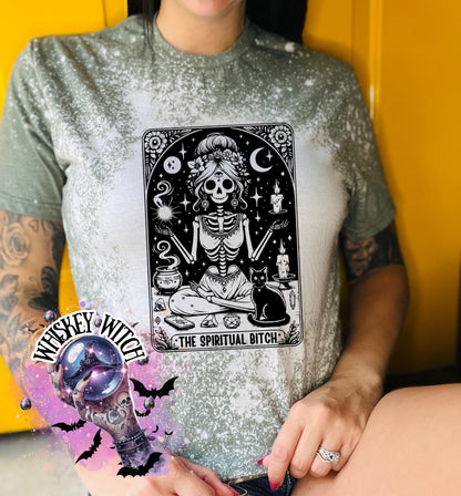 A bleached military green t-shirt with a black and white illustration of a skeleton woman with a cat and the text "The Spiritual Bitch".