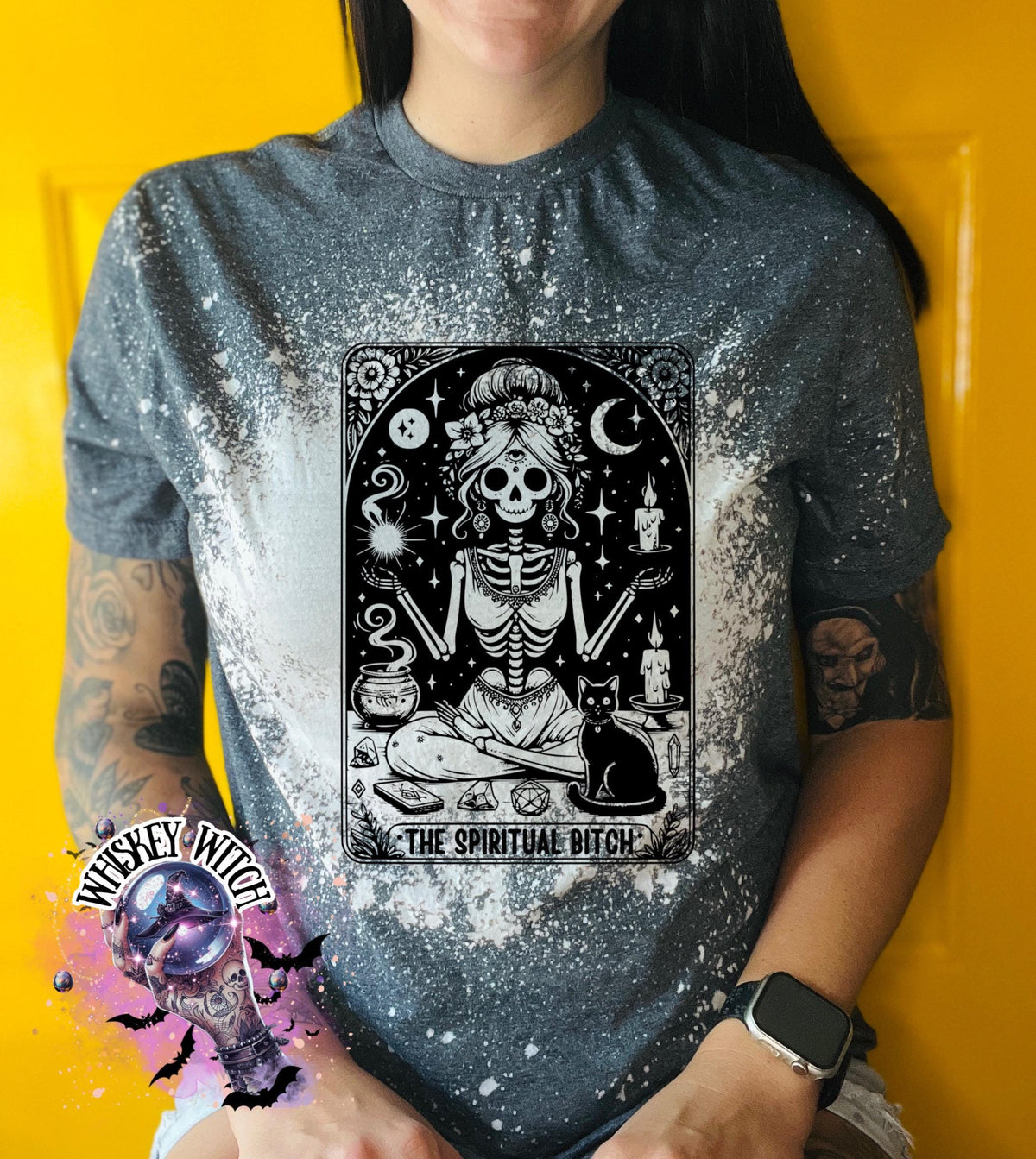 A bleached grey t-shirt with a black and white illustration of a skeleton woman with a cat and the text "The Spiritual Bitch".
