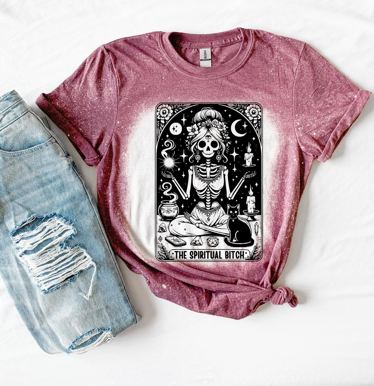 A bleached maroon t-shirt with a black and white illustration of a skeleton woman with a cat and the text "The Spiritual Bitch".