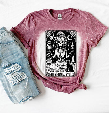A bleached maroon t-shirt with a black and white illustration of a skeleton woman with a cat and the text "The Spiritual Bitch".
